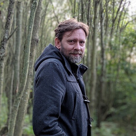 Writer Karl Hughes torso shot with wooded backdrop